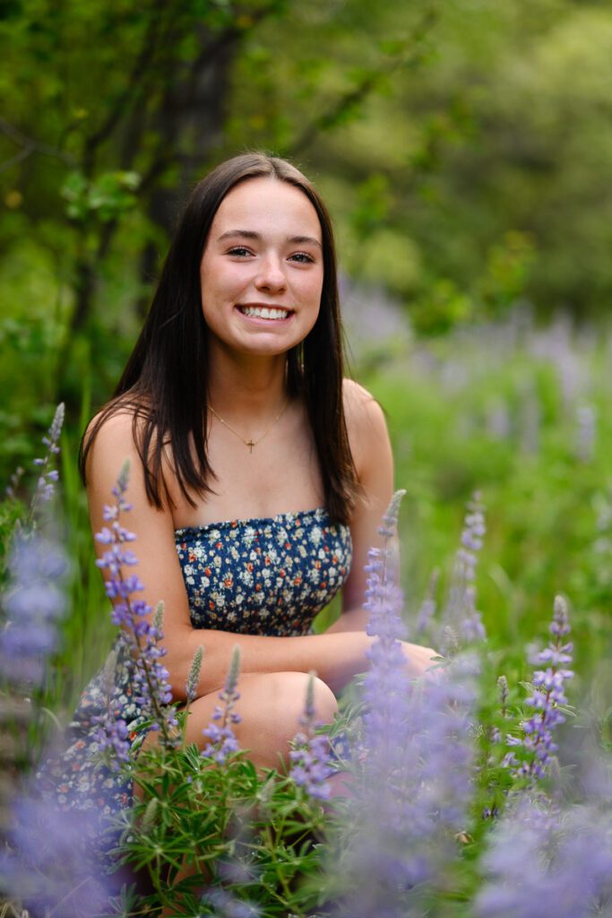 Sitting in a field of purple wildflowers a girl smiles at her Denver colorado senior photographer for her Aspen senior photos