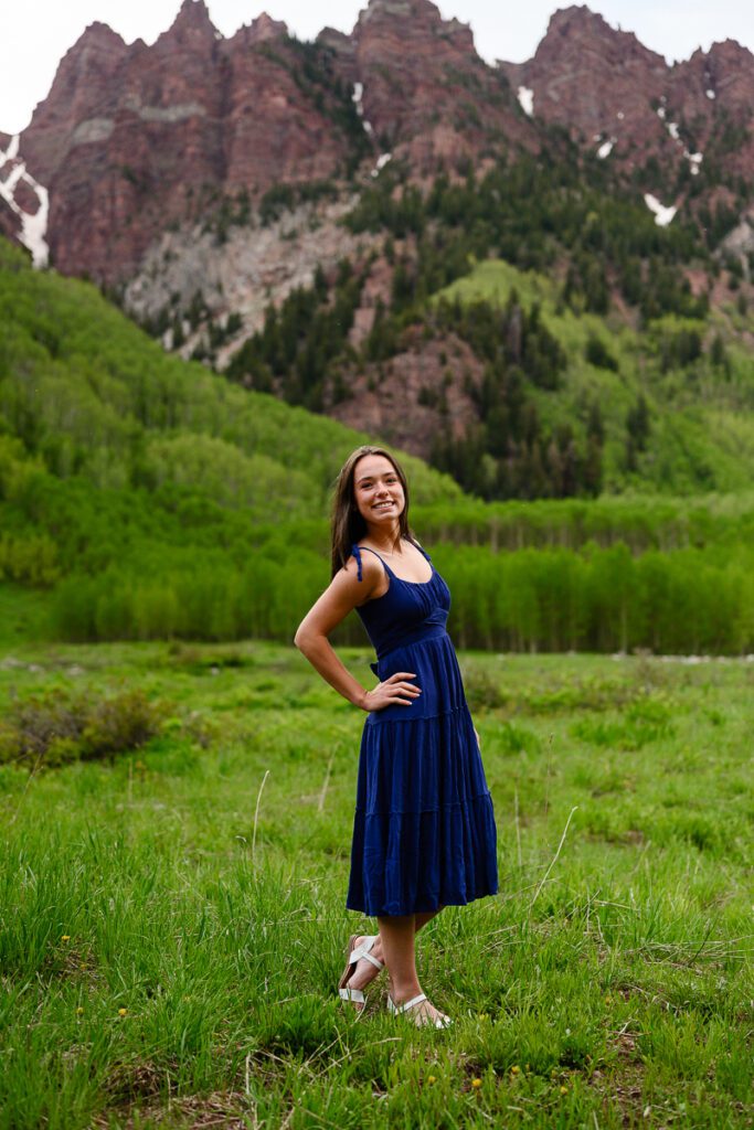 Beautiful senior girl in a blue dress against the green fields of the maroon bells in Aspen Colorado as captured by Denver senior photographer