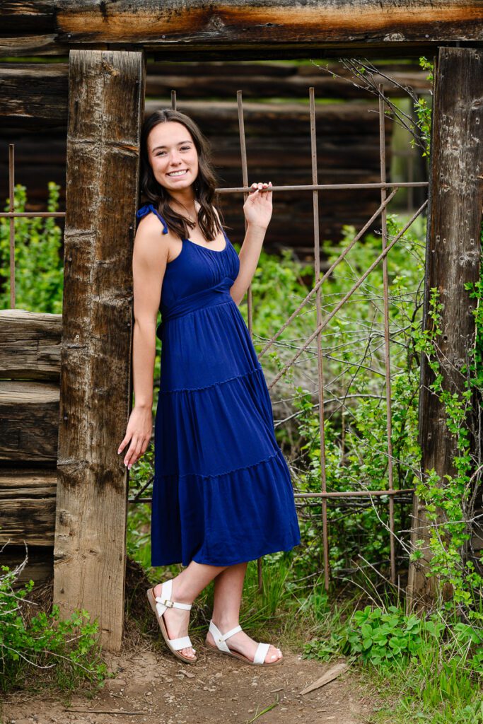 A senior girl in a blue dress smiles at a Denver senior photographer at the Ashcroft ghost town in Aspen Colorado