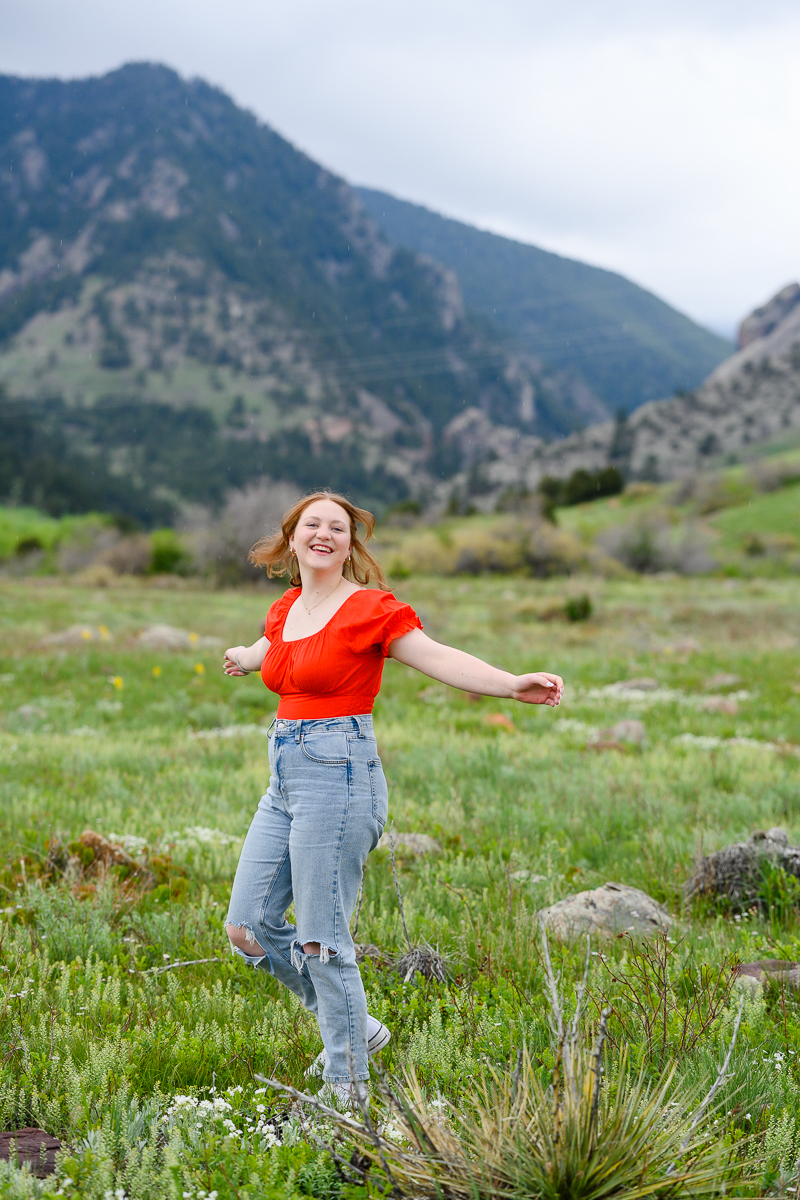 denver senior photographer photographs senior girl dancing in a wild flower field in the mountains while wearing a red top and blue jeans