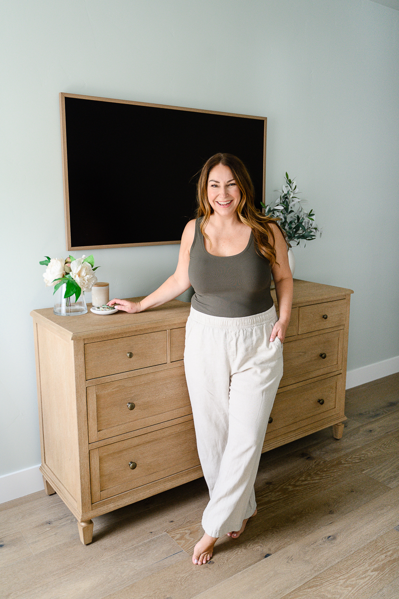 Denver commercial photographer photographs woman in neutral outfit standing next to a dresser with one of her hands on the top of the dresser