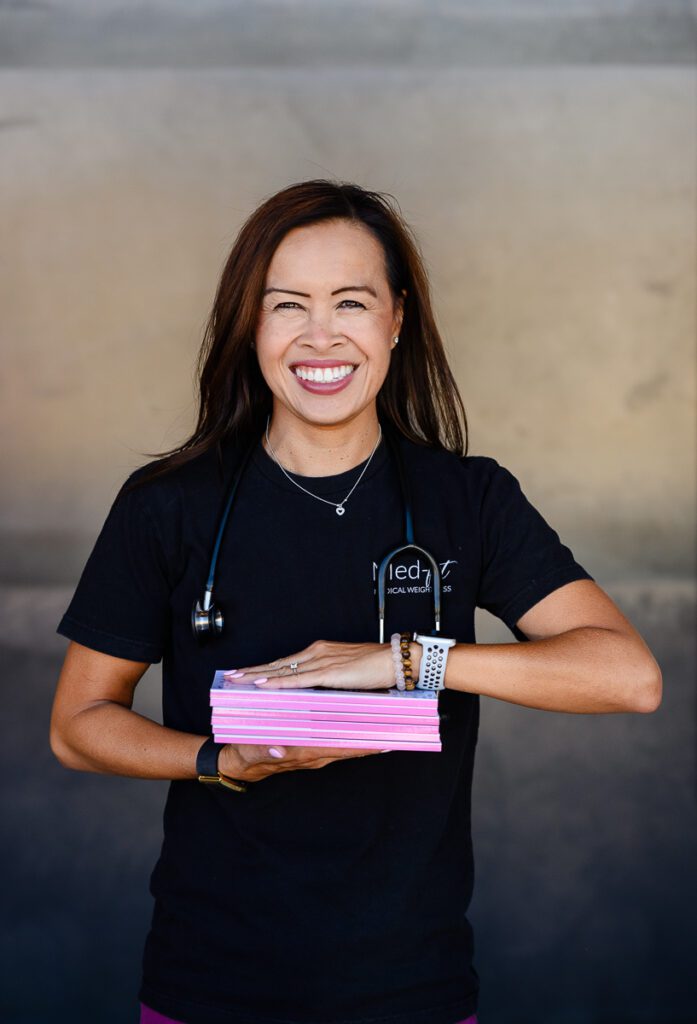 A doctor in black scrubs holding a stack of books smiling at a Denver Commercial Photographer