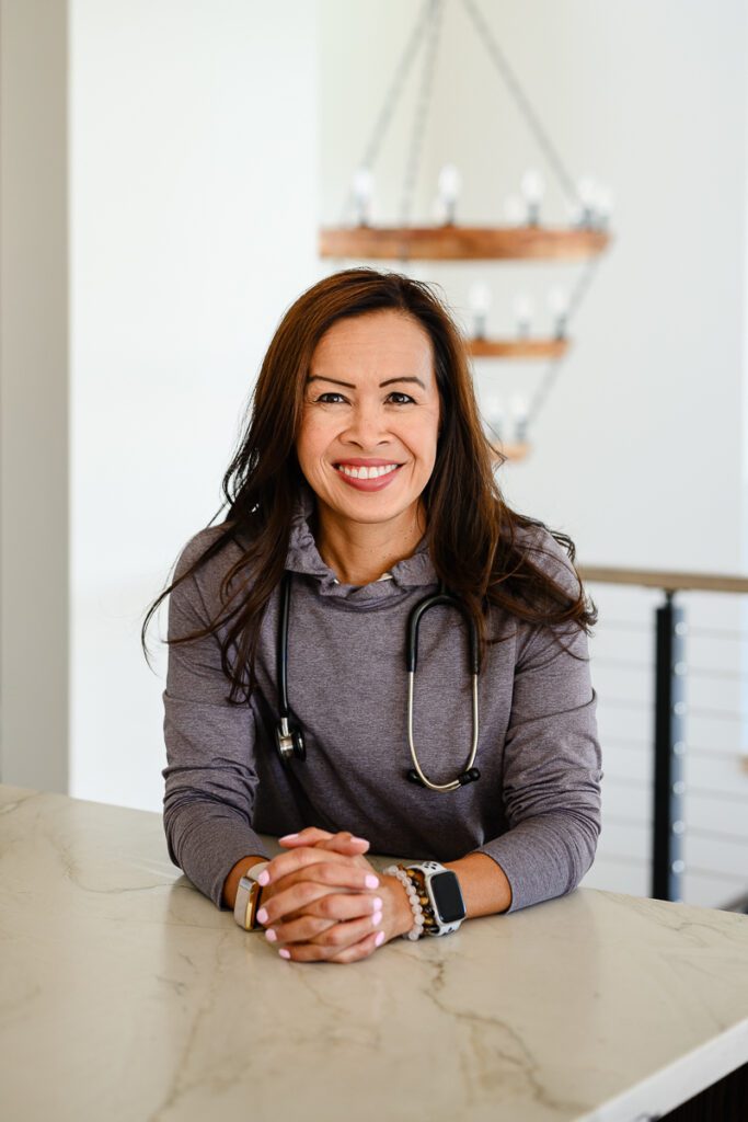 A woman doctor with a stethescope leans on the counter and smiles for her Denver branding photos.