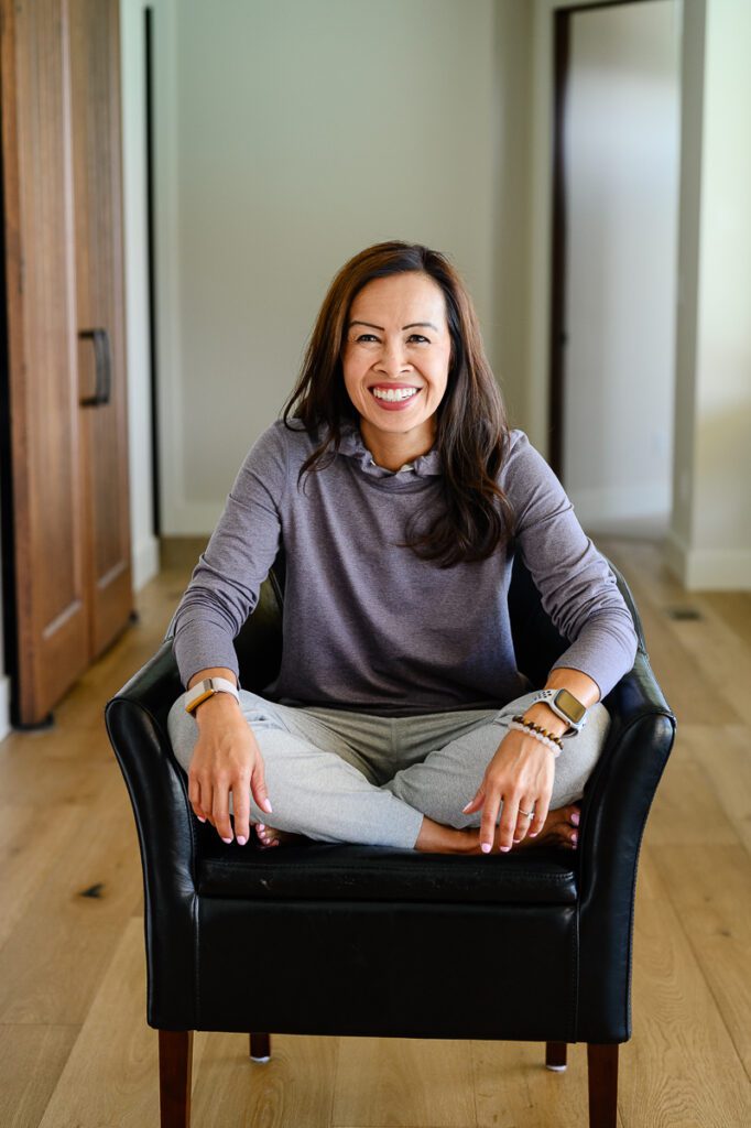 A woman smiles at her Denver Branding photographer while sitting in a black chair wearing cozy clothes.