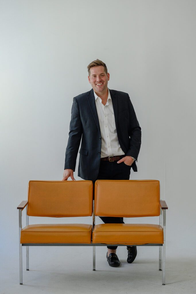 A Denver branding photographer captures a man leaning on an orange couch in a suit.