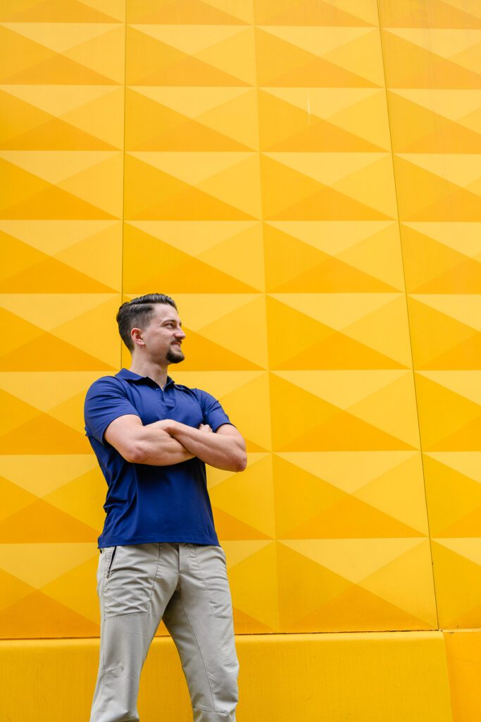 A denver branding photographer takes a picture of a man for his branding photos in front of a textured yellow wall.
