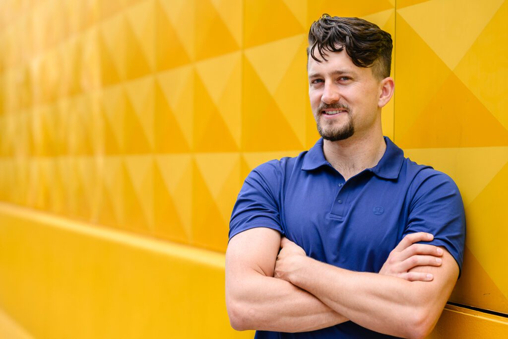 A man poses for his Denver Branding Photos in front of a yellow wall.