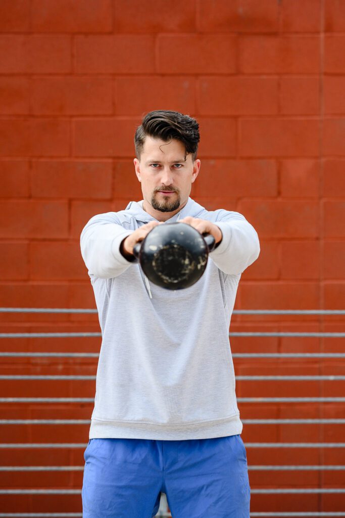 A man with a kettle bell stares into the eyes of the Denver Branding Photographer for his fitness branding photos.