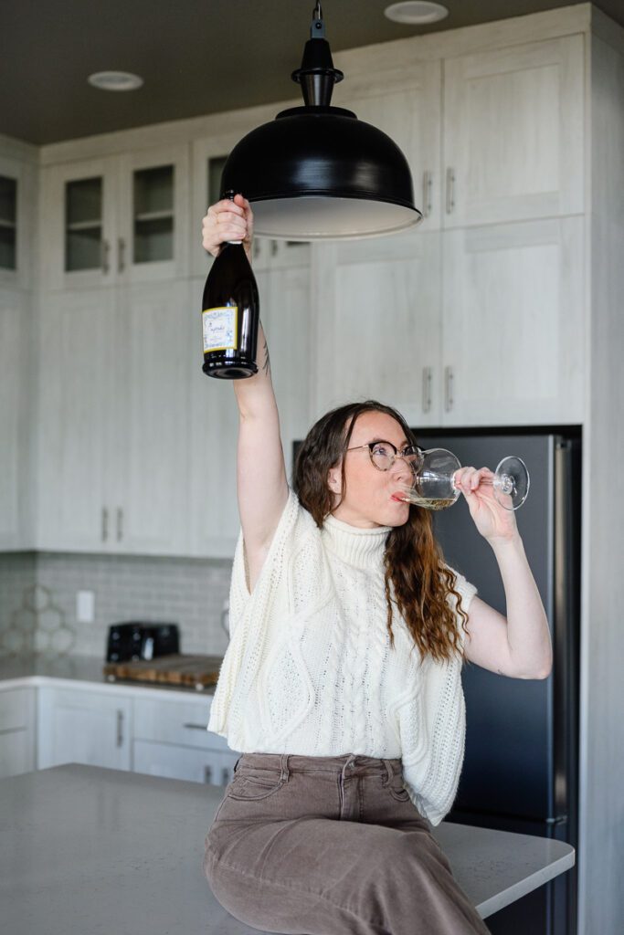A woman drinking champagne and holding up a glass for a branding coach.
