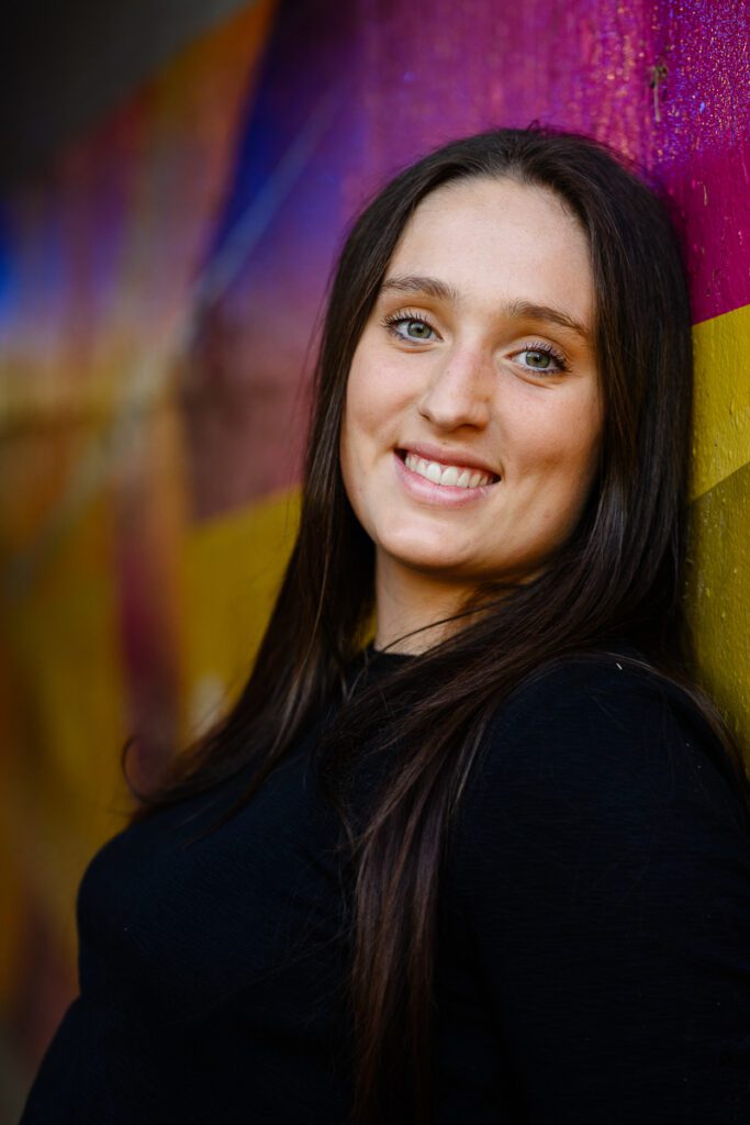 A close up of a young woman against a colorful mural smiling at a Denver Photographer.
