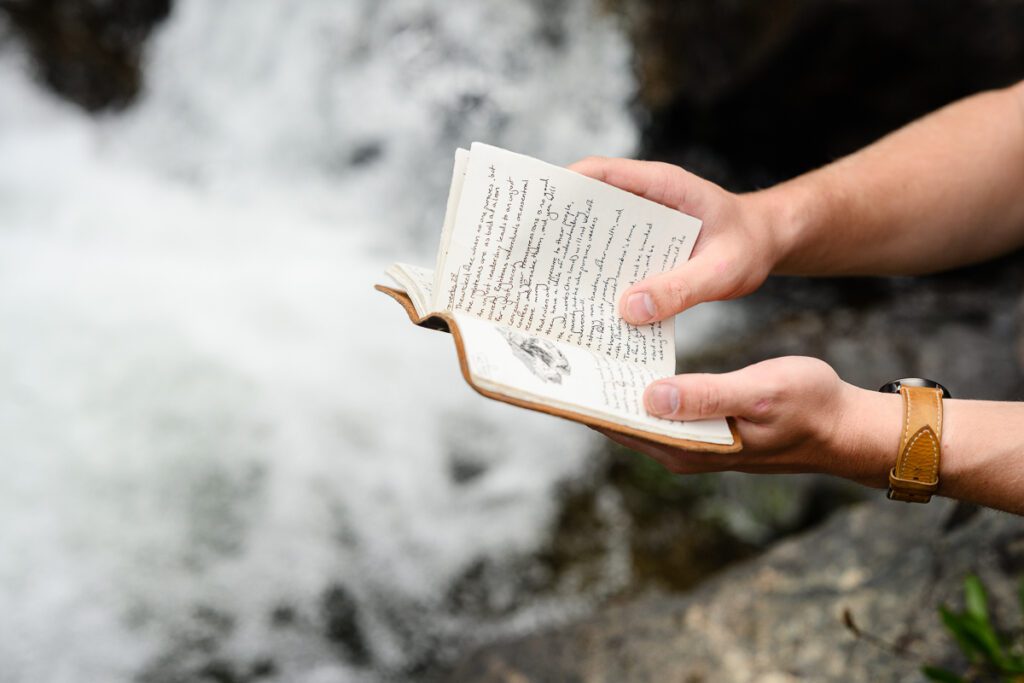 A closeup of a man holding a leather journal with a raging river in the background as captured by a Denver Branding Photographer for branding photos for a small business owner.