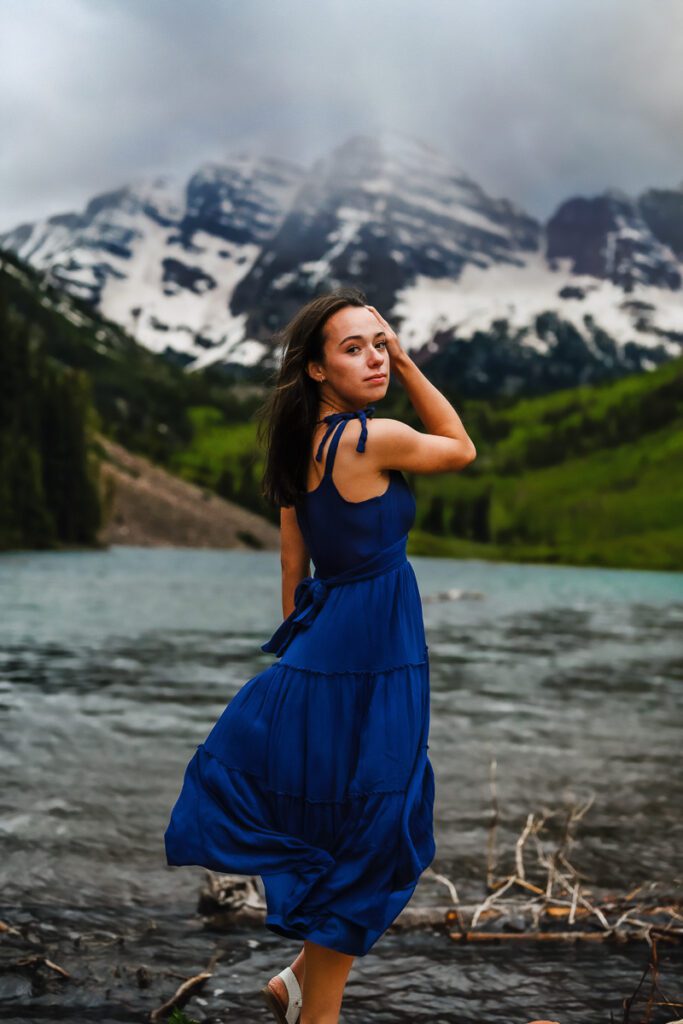 A young girl in a blue dress standing in front of the Maroon Bells in Aspen for her senior pictures as captured by a Denver photographer for Denver senior pictures.
