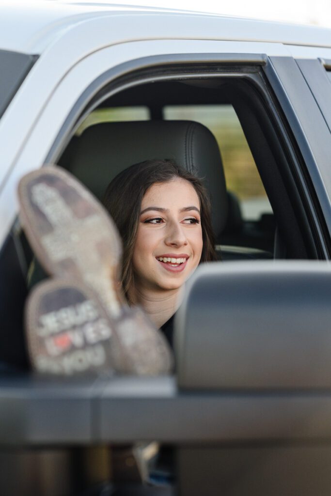 A young woman with her feet up on a white truck window with the bottom of her boots saying Jesus Loves you as captured by a Denver photographer and brand coach.