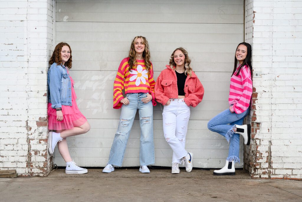 4 senior girls in bright colors standing in front of a white door as captured by a Denver photographer and brand strategist.
