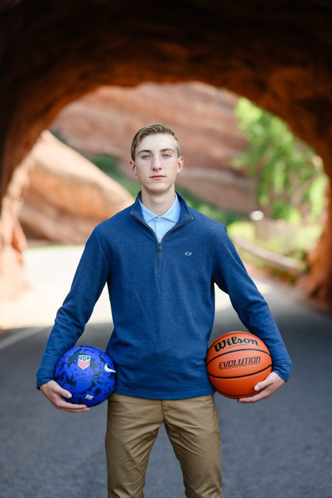 A senior holding a basketball and soccer ball at Red Rocks Amphitheater captured by a Denver photographer and branding strategist.