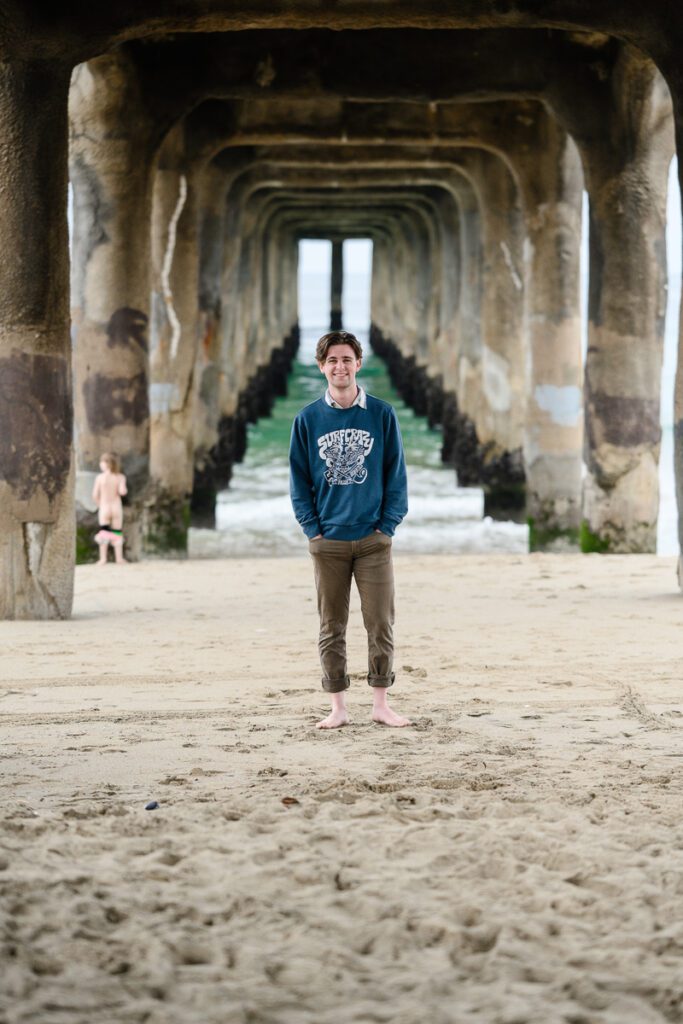 A man standing under a pier in California captured by a Denver Branding Photographer for his Denver senior pictures.