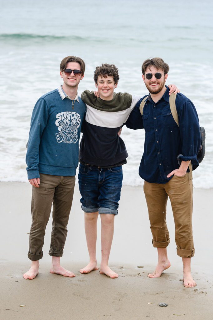 3 young men standing on the beach smiling at a Denver photographer
