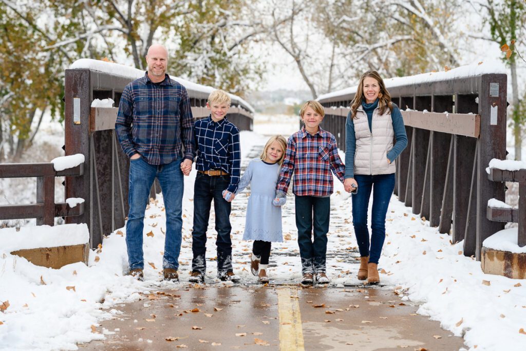 A family standing on a bridge in the snow smiling at a Denver branding photographer.