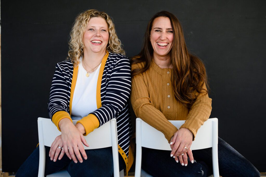 2 women sitting backwards on chairs smiling at a Denver branding photographer for their branding photos during their branding consulting with a Denver brand coach and strategist.