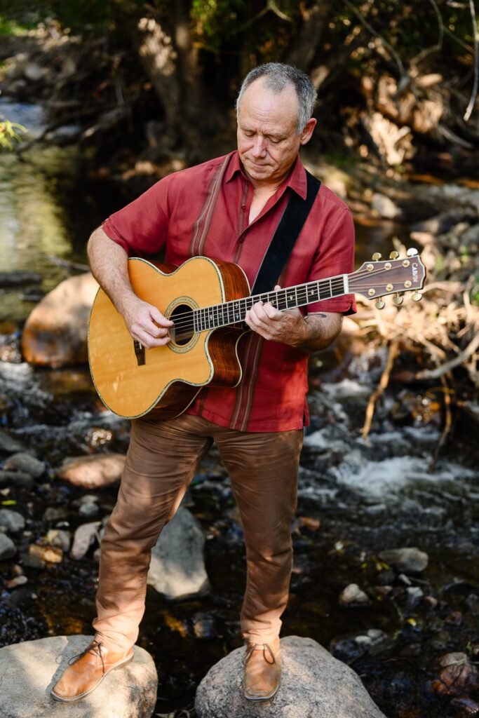 A musician standing near a river bank playing guitar captured by a Denver branding photographer and brand strategist.