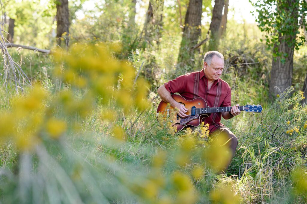 A Denver branding photographer and brand strategist captures a musician sitting on a chair in a field with yellow flowers in the foreground with his guitar.