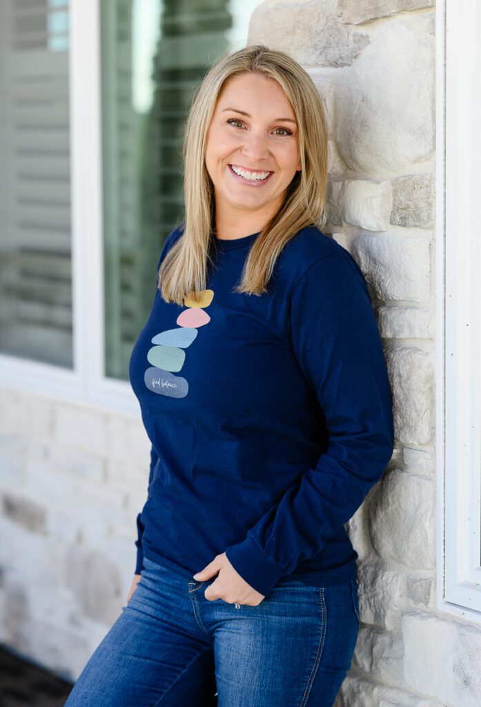 A blonde small business owner standing against a stone wall smiling at a Denver branding photographer and brand strategist.