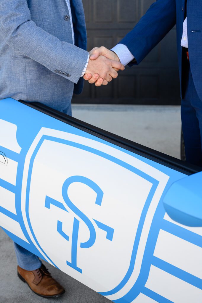 Two men shaking hands by a blue Lamborghini with the letters ST on the door as captured by a Denver branding photographer and branding coach.