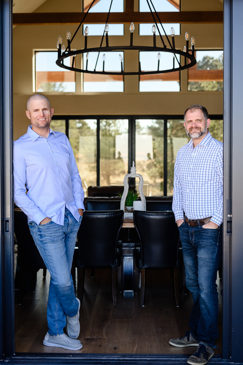 Two men in blue button down shirts leaning on an outdoor patio door smiling at a Denver branding photographer and branding consultant.