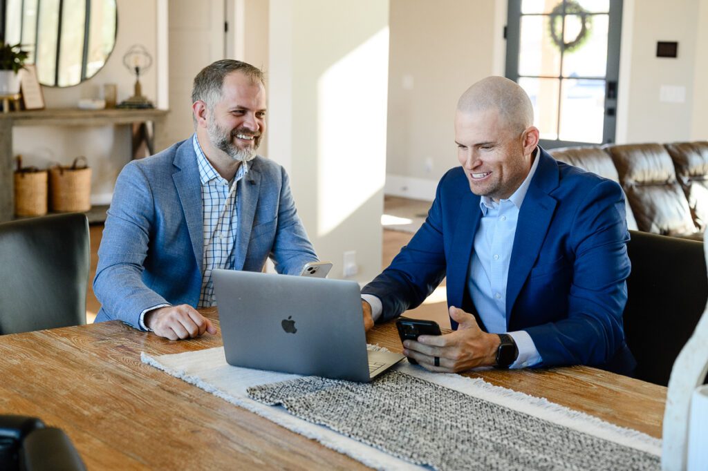 2 men in suits sitting at a table looking at a computer with stock information for their Denver Branding Photos by their branding strategist.