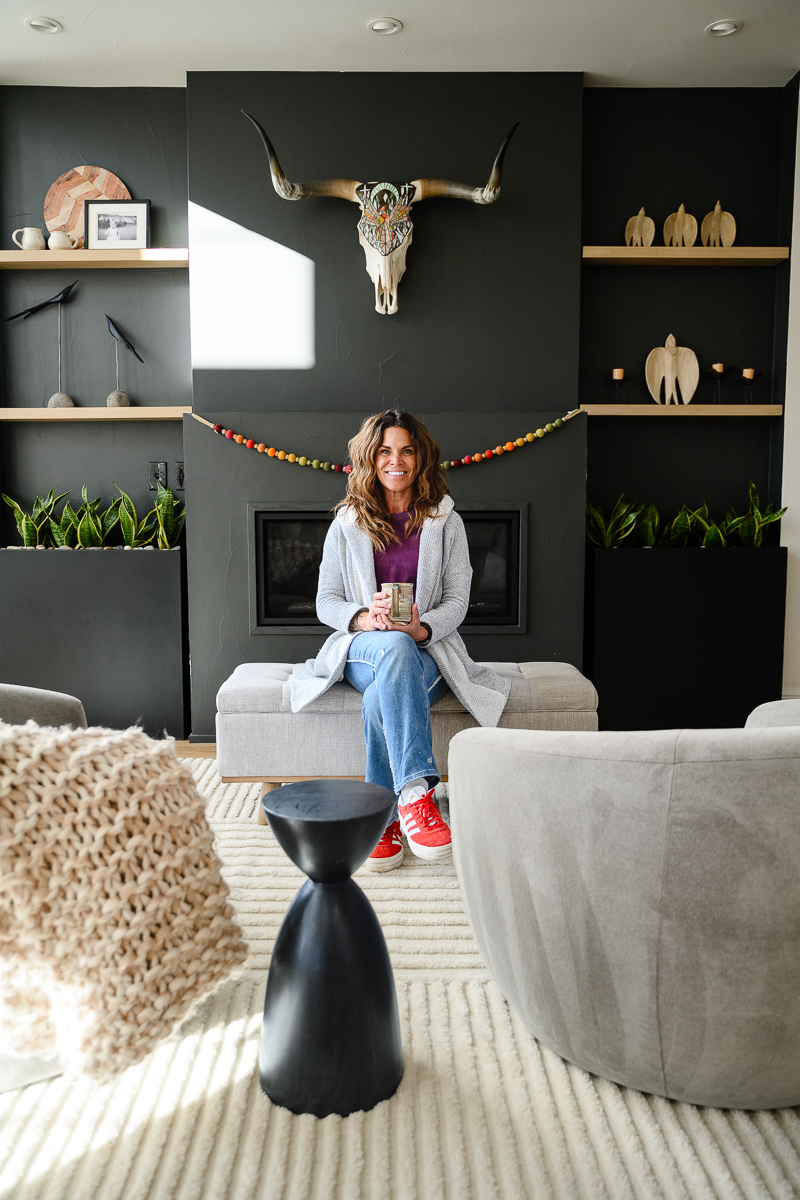 Consistent branding with brand photographer in Denver photographing a woman sitting on a coffee table in front of a black fireplace at a Boho studio session for brand photo