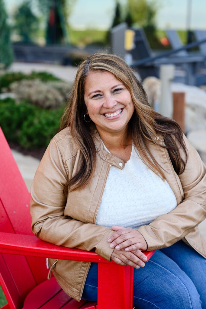 Branding photo shoot for office team with woman sitting in a red chair holding her hands together on the armrest and smiling at brand photographer