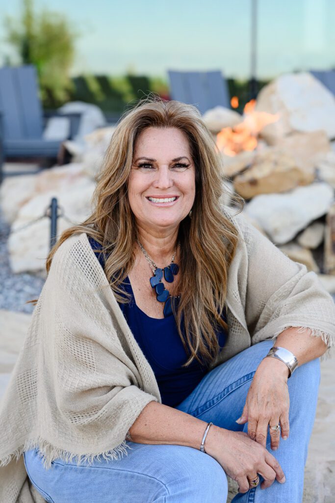 Business head shot photographed by brand photographer of woman in a beige cardigan and a dark blue shirt posing on a stone patio