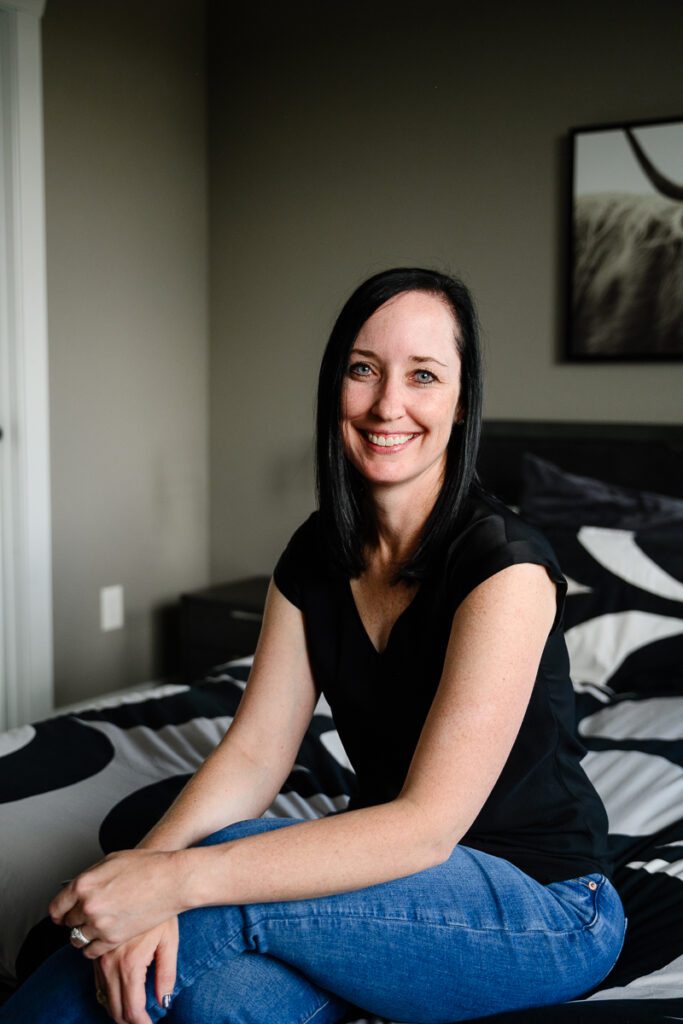 A small business owner and entrepreneur sits on a bed and smiles at a Denver Branding photographer for her strategic branding photos.