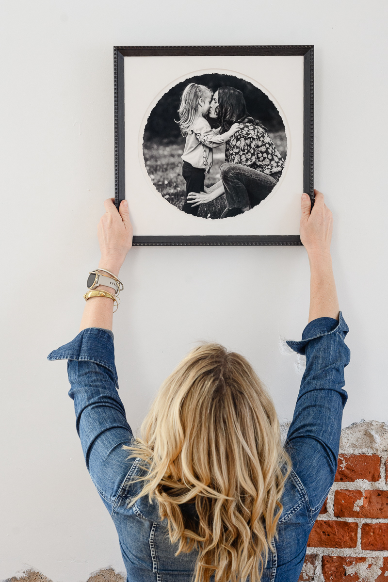 brand photographer holds up a square picture frame withe a circle picture in it of a mother kissing her child