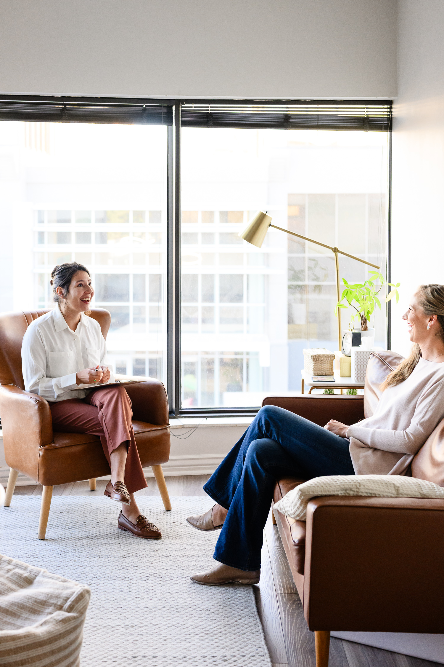 A wellness professional smiles while speaking with a client in a bright, modern office space, capturing a fresh brand image that avoids outdated branding, taken by a Denver brand photographer