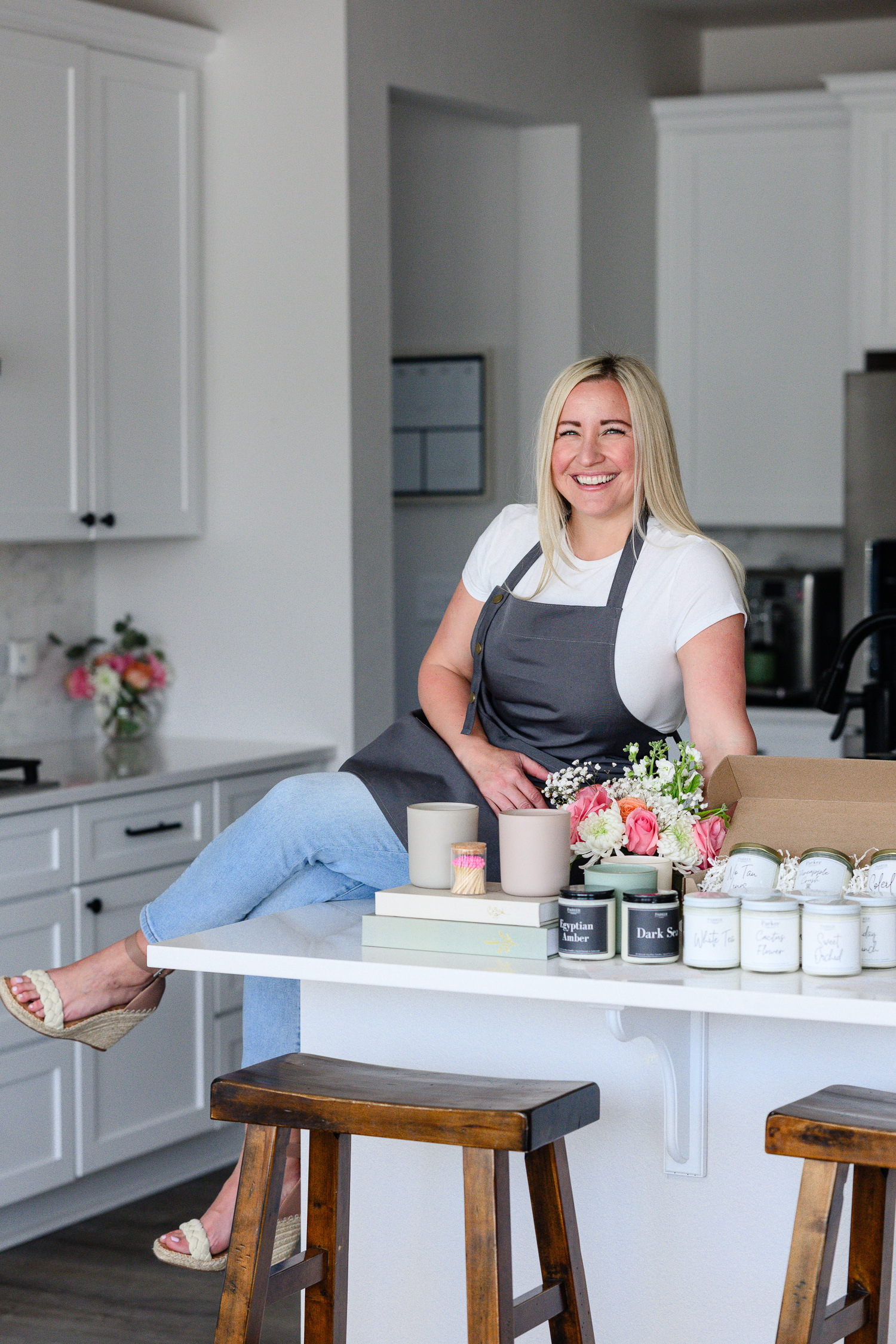 Candle maker sitting on a kitchen counter with an assortment of labeled candles, packaging, and flowers, showcasing a clean, cohesive aesthetic that reflects maintaining brand consistency; photographed by Denver commercial photographer.