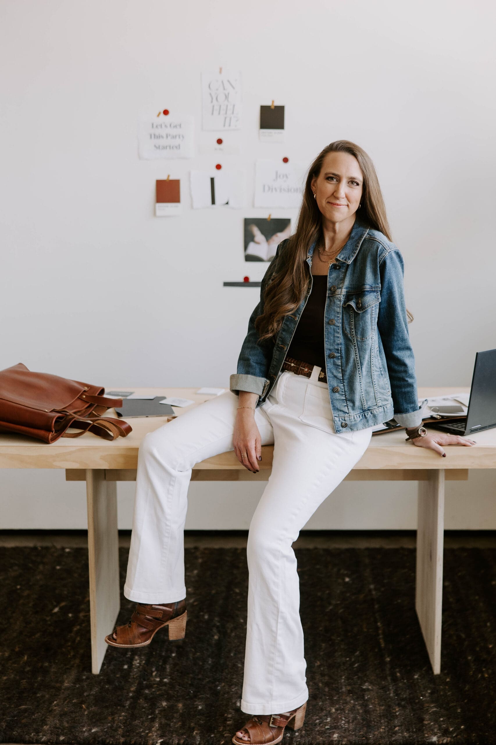 Denver branding photographer seated on a desk in a creative workspace, highlighting professional brand photography and personal branding expertise.
