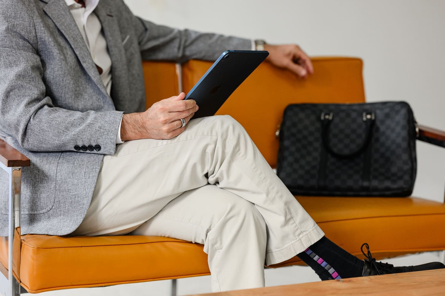 Professional seated on a modern tan leather chair holding a tablet, with a black briefcase in the background, showcasing a polished business environment often captured by a **denver brand photographer** for personal branding and corporate marketing content.