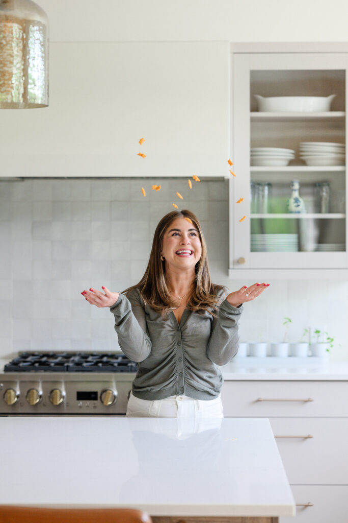 Woman tossing colorful sprinkles into the air in a bright, modern kitchen, capturing a fun and playful lifestyle moment that showcases personality and authentic brand photography by a Denver photographer.