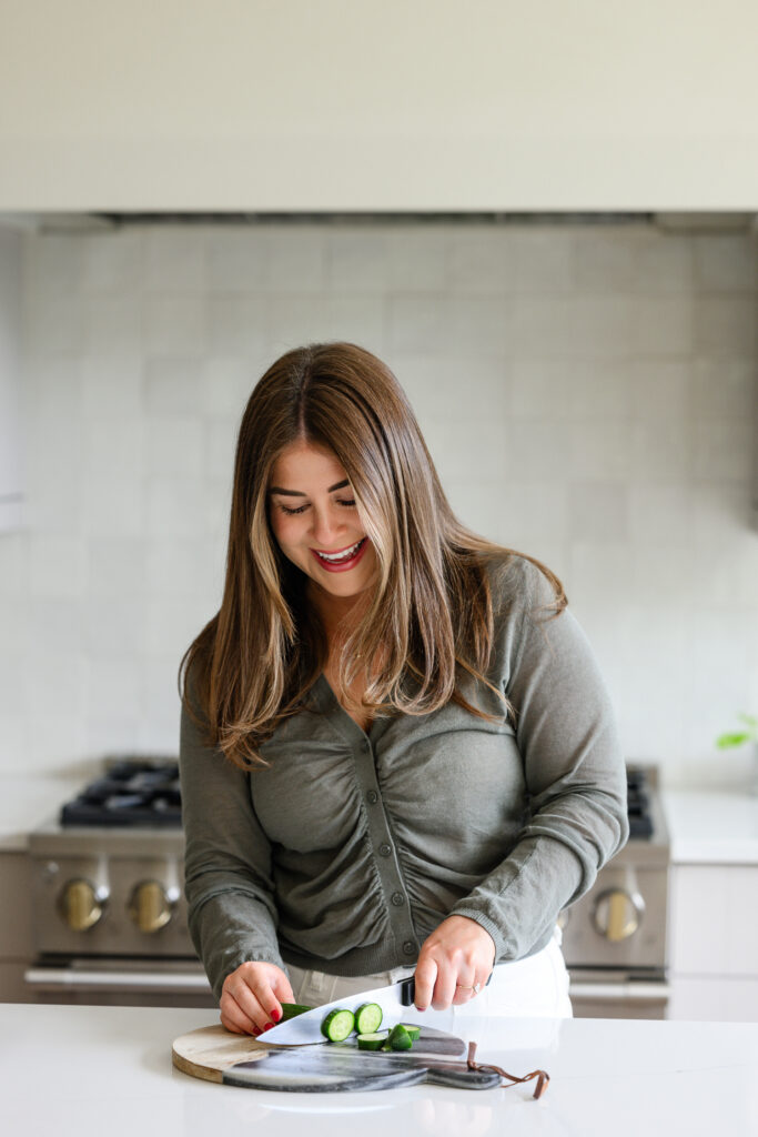 Woman preparing fresh cucumber slices on a cutting board in a bright, modern kitchen, capturing an authentic healthy lifestyle moment for brand photography by a Denver photographer.