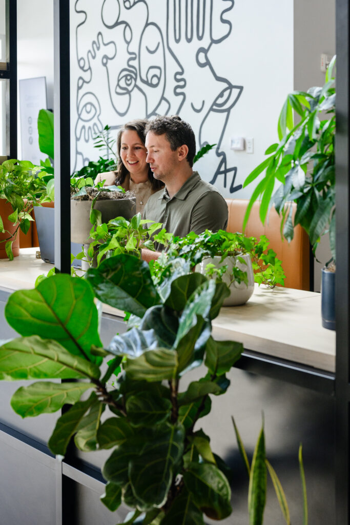 Two business owners collaborate at a table surrounded by lush indoor plants and modern artwork during a denver branding session, with a branding photographer creating natural website photography that highlights their workspace.