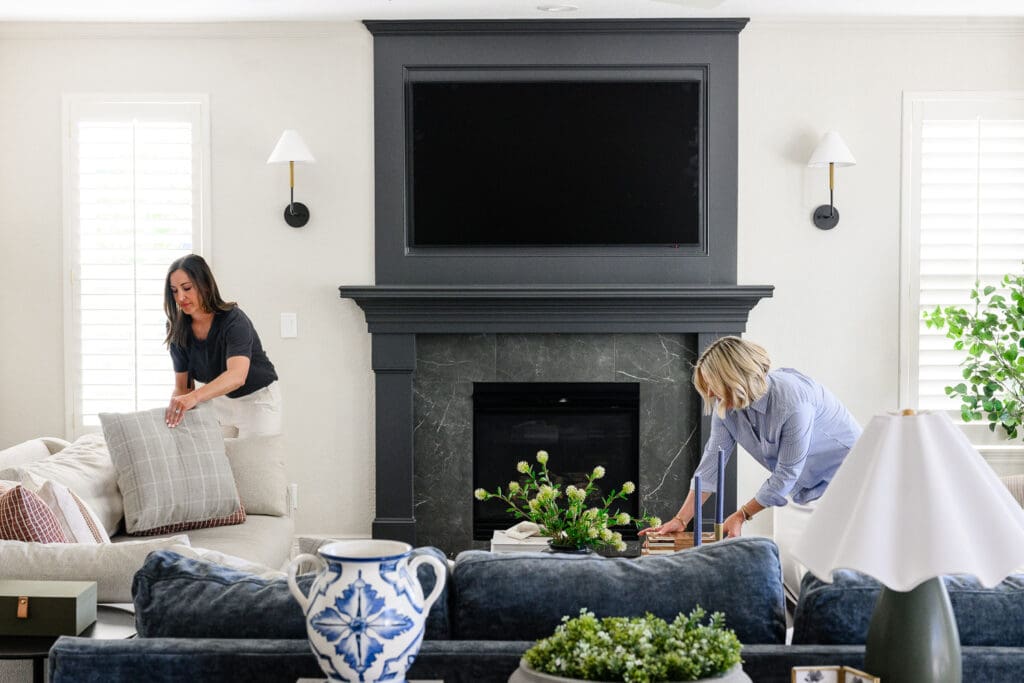 Two interior designers styling pillows and decor in a bright living room, creating behind-the-scenes branding photography that highlights their interior design process.