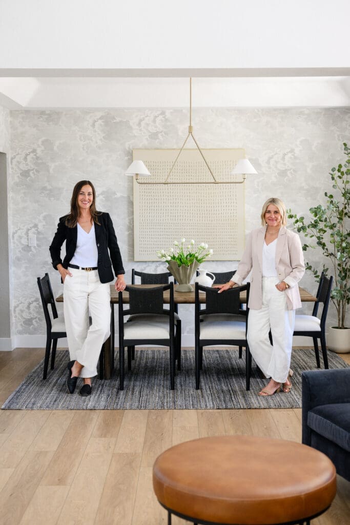 Two interior designers photographed in a styled dining room with textured wallpaper, modern furnishings, white florals, and statement lighting for branding for interior designers.