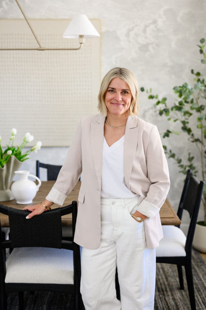 Interior designer portrait beside a styled dining table, wearing a neutral blazer in a light-filled interior during a branding photography session.