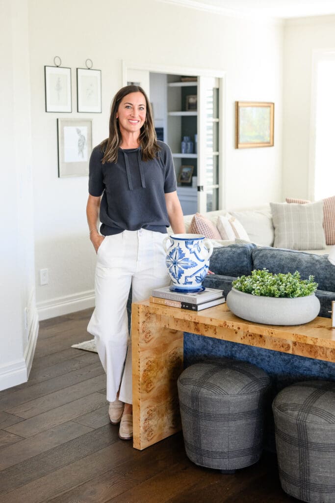 Interior designer standing beside a styled burl wood console and blue velvet sofa during a denver brand photographer session showcasing her work and personal brand.