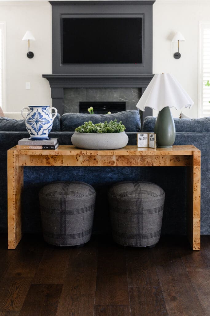 Layered living room featuring a burl wood console, blue velvet sofa, patterned stools, ceramic decor, and statement fireplace captured through branding photography.